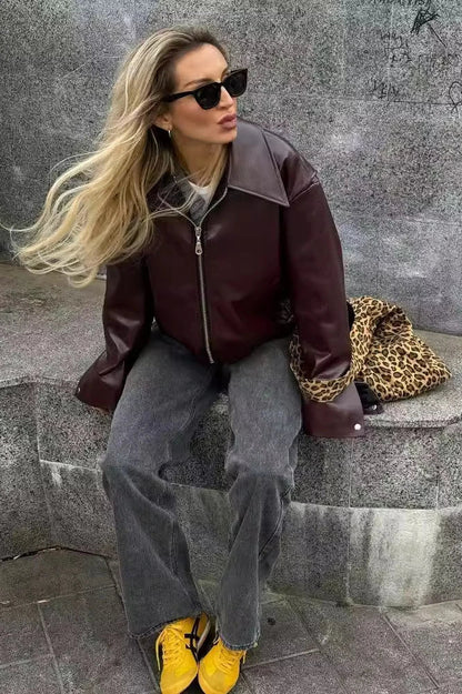 Woman in burgundy faux leather bomber jacket and black jeans.