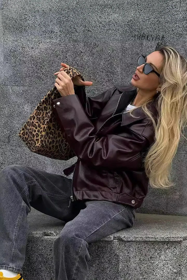 Woman in burgundy faux leather bomber jacket and black jeans.
