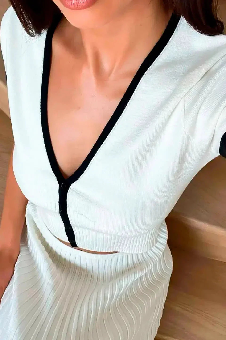 Woman in white ribbed knit crop top and pleated skirt with black trim standing on stairs.
