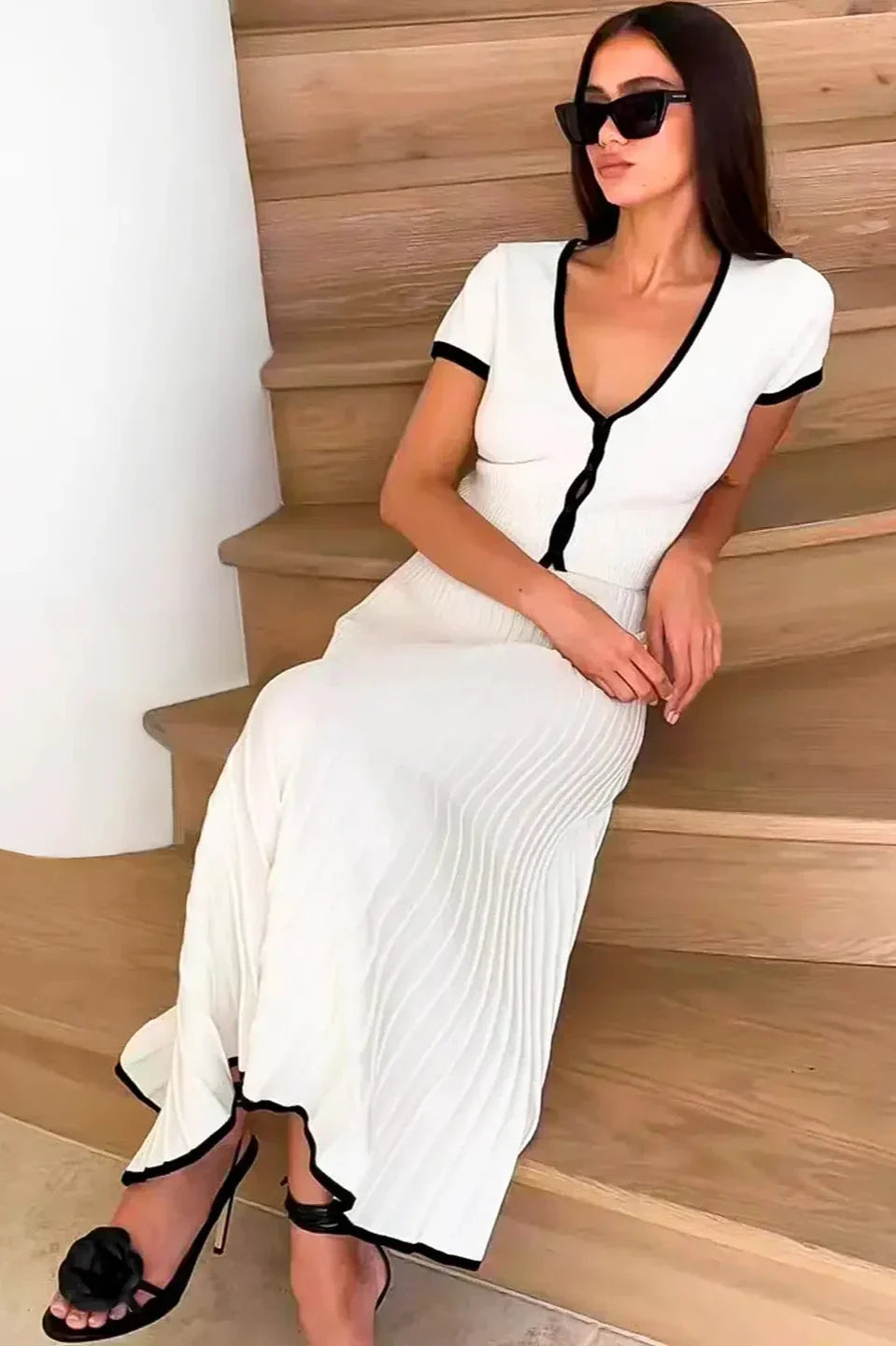 Woman in white ribbed knit crop top and pleated skirt with black trim standing on stairs.