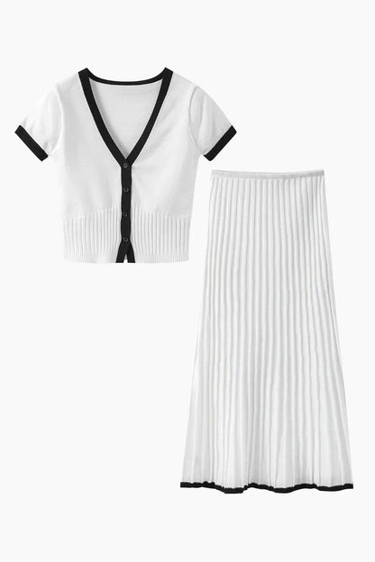 Woman in white ribbed knit crop top and pleated skirt with black trim standing on stairs.