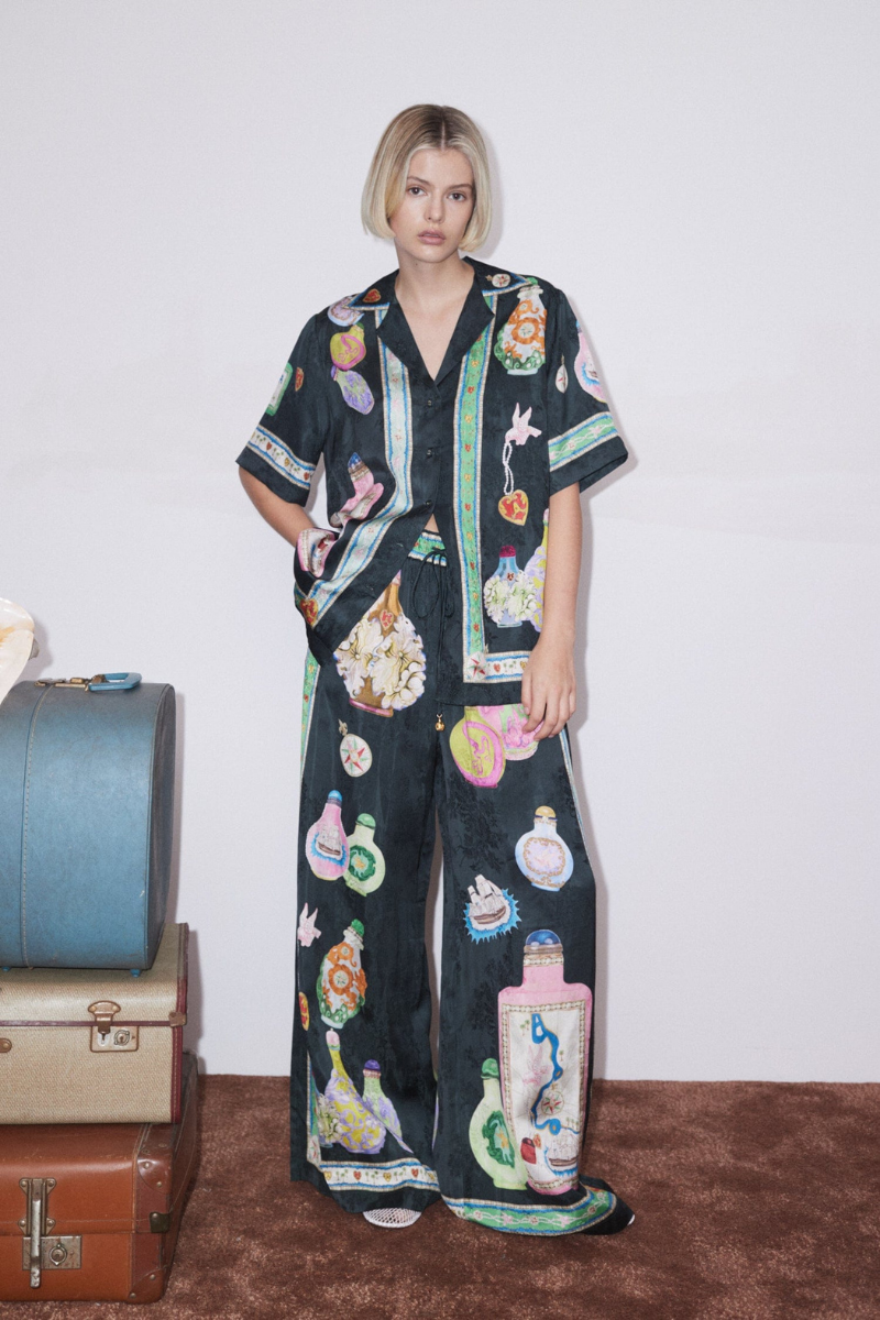 Woman wearing black silk pajama set with colorful bottle print.