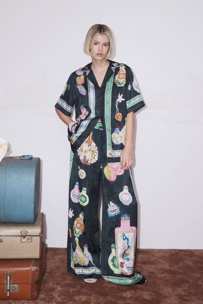 Woman wearing black silk pajama set with colorful bottle print.