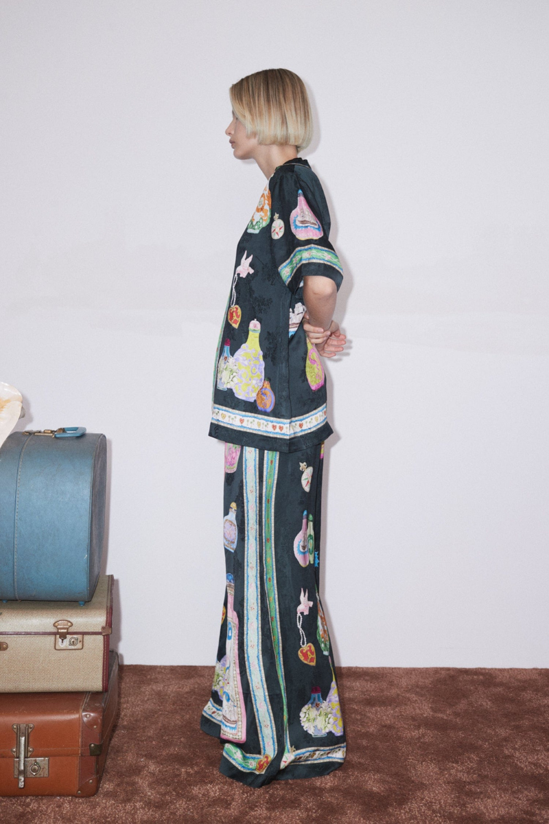 Woman wearing black silk pajama set with colorful bottle print.