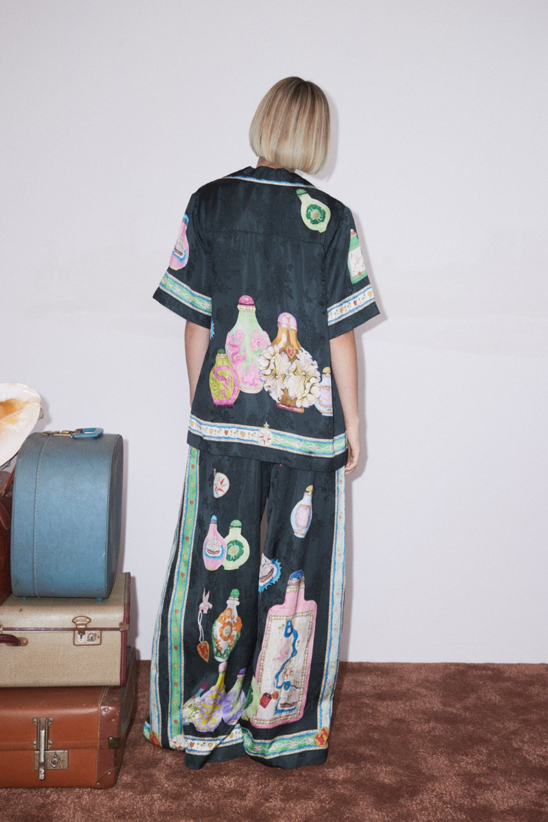 Woman wearing black silk pajama set with colorful bottle print.