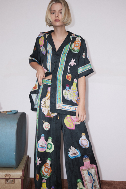 Woman wearing black silk pajama set with colorful bottle print.