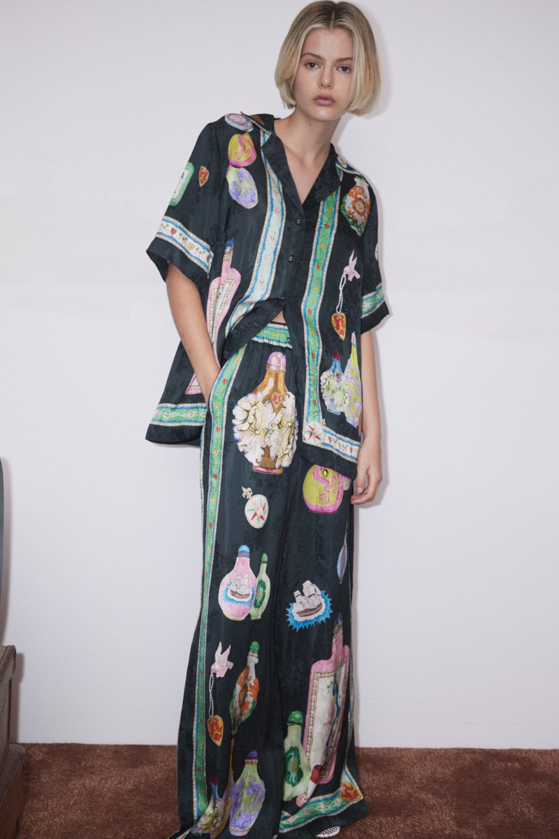 Woman wearing black silk pajama set with colorful bottle print.