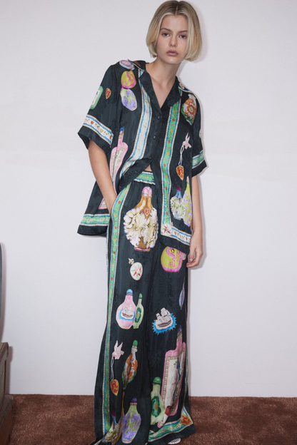Woman wearing black silk pajama set with colorful bottle print.