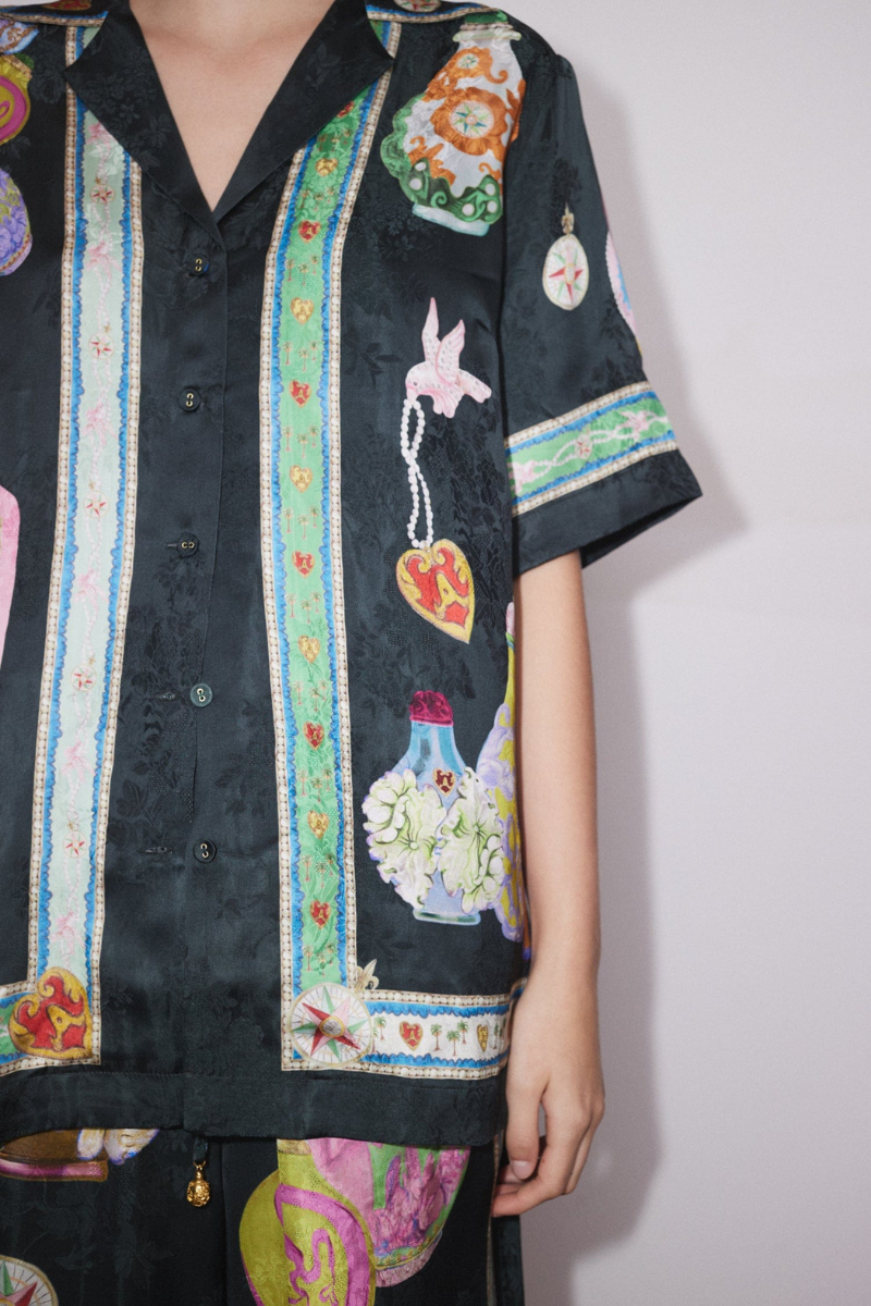 Woman wearing black silk pajama set with colorful bottle print.