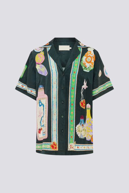 Woman wearing black silk pajama set with colorful bottle print.
