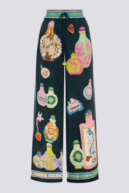 Woman wearing black silk pajama set with colorful bottle print.