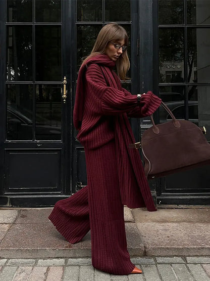 Woman in burgundy ribbed knit sweater and wide leg pants carrying a brown suede bag.