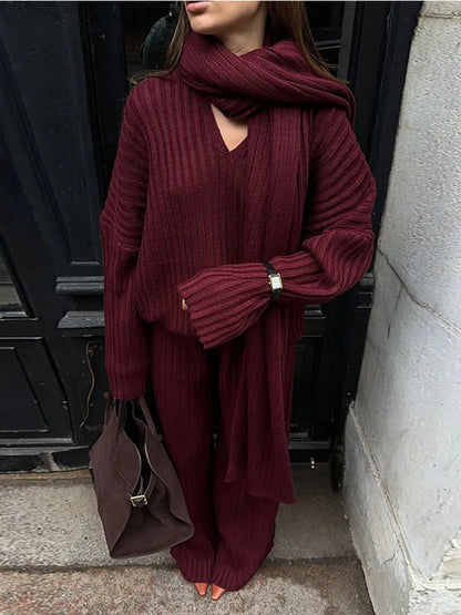 Woman in burgundy ribbed knit sweater and wide leg pants carrying a brown suede bag.