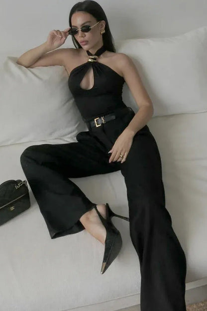 Woman wearing a black jersey halter top with gold hardware detail.