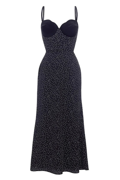 Woman in black polka dot midi dress with velvet bodice leaning against white wall