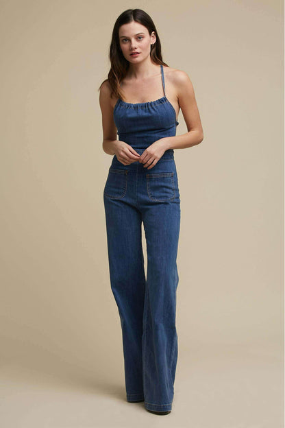 Woman in a blue denim jumpsuit with a halter neck and wide legs.