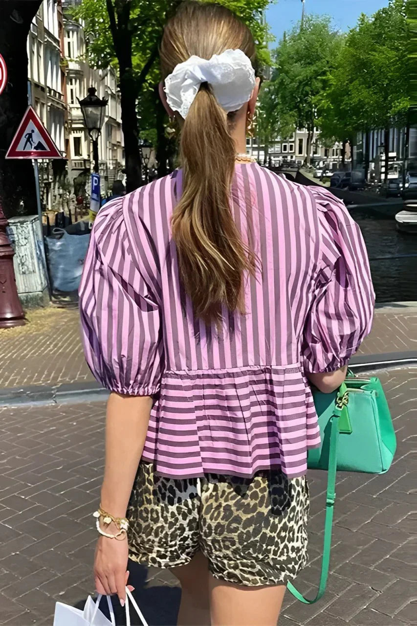 Woman in pink and brown striped blouse and khaki shorts holding sunglasses