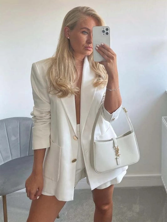 Woman in white linen blazer and shorts taking a selfie.