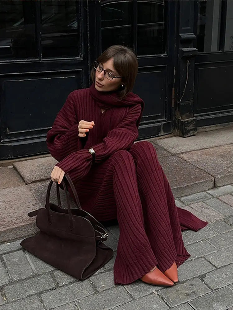Woman in burgundy ribbed knit sweater and wide leg pants carrying a brown suede bag.