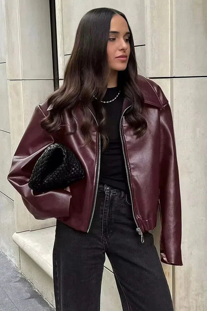 Woman in burgundy faux leather bomber jacket and black jeans.