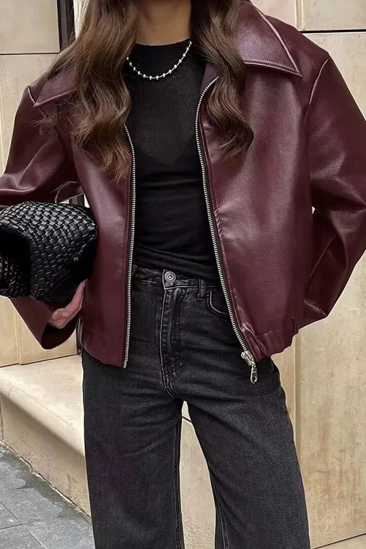 Woman in burgundy faux leather bomber jacket and black jeans.