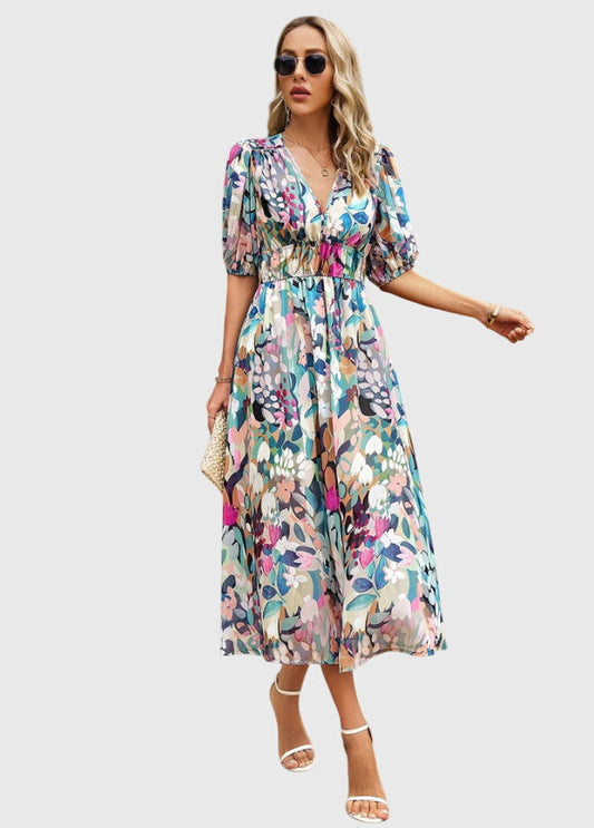 Floral - A woman wearing a vibrant multi-color abstract floral print chiffon midi dress with puff sleeves, a V-neckline, and a smocked waist, paired with white heeled sandals.