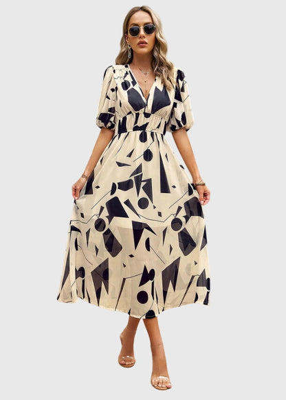Apricot - A woman wearing a vibrant multi-color abstract floral print chiffon midi dress with puff sleeves, a V-neckline, and a smocked waist, paired with white heeled sandals.