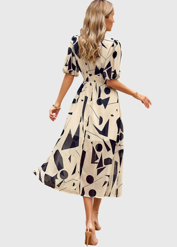 Apricot - A woman wearing a vibrant multi-color abstract floral print chiffon midi dress with puff sleeves, a V-neckline, and a smocked waist, paired with white heeled sandals.