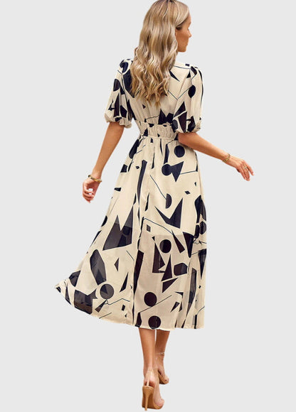 Apricot - A woman wearing a vibrant multi-color abstract floral print chiffon midi dress with puff sleeves, a V-neckline, and a smocked waist, paired with white heeled sandals.