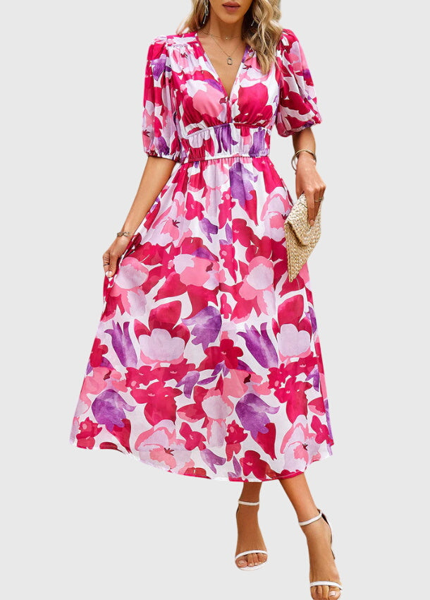 Apricot - A woman wearing a vibrant multi-color abstract floral print chiffon midi dress with puff sleeves, a V-neckline, and a smocked waist, paired with white heeled sandals.