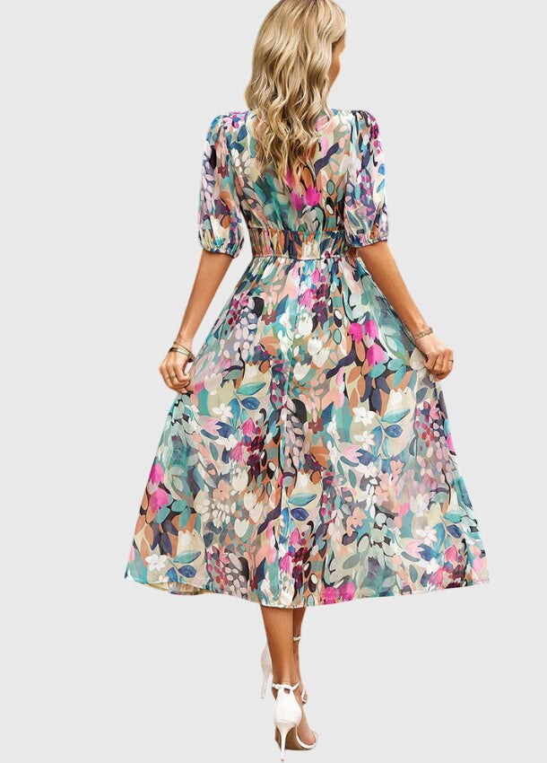 Floral - A woman wearing a vibrant multi-color abstract floral print chiffon midi dress with puff sleeves, a V-neckline, and a smocked waist, paired with white heeled sandals.