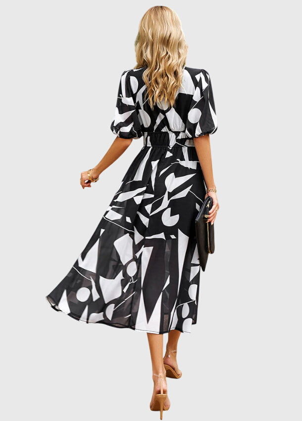 Black - A woman wearing a vibrant multi-color abstract floral print chiffon midi dress with puff sleeves, a V-neckline, and a smocked waist, paired with white heeled sandals.