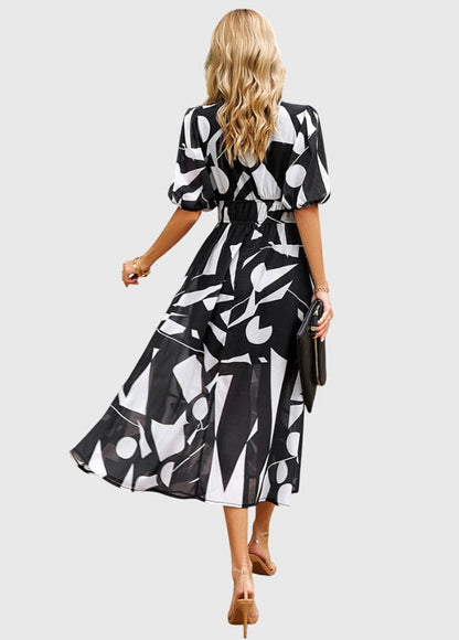 Black - A woman wearing a vibrant multi-color abstract floral print chiffon midi dress with puff sleeves, a V-neckline, and a smocked waist, paired with white heeled sandals.