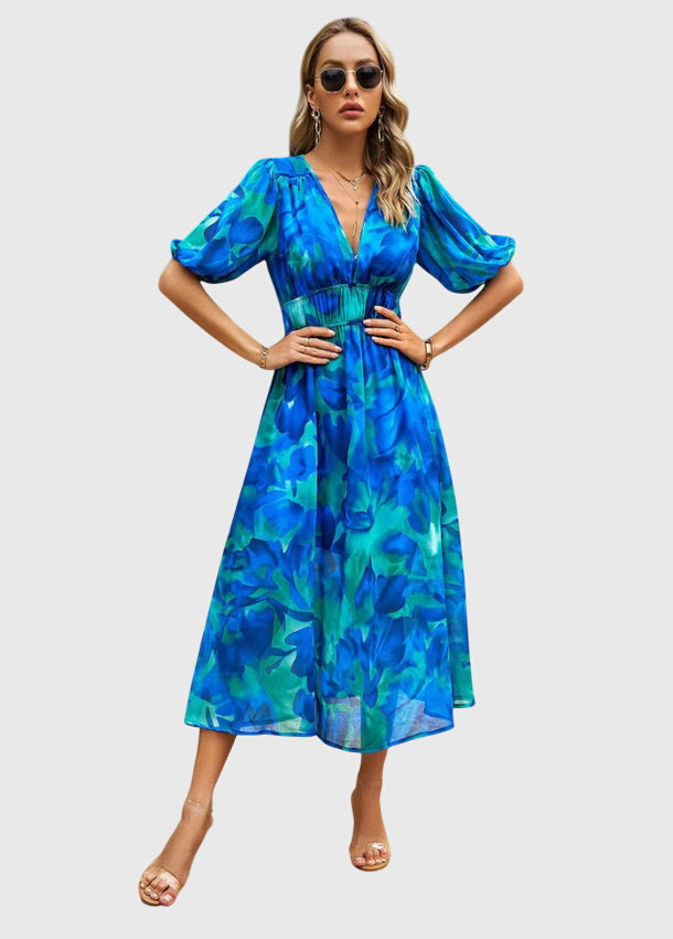 Blue - A woman wearing a vibrant multi-color abstract floral print chiffon midi dress with puff sleeves, a V-neckline, and a smocked waist, paired with white heeled sandals.