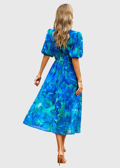 Blue - A woman wearing a vibrant multi-color abstract floral print chiffon midi dress with puff sleeves, a V-neckline, and a smocked waist, paired with white heeled sandals.