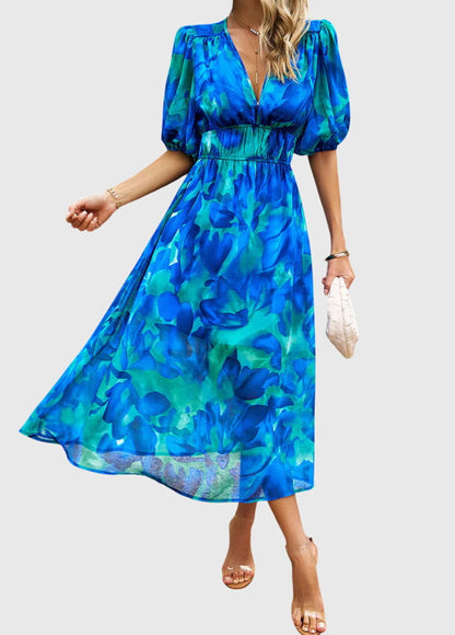 Blue - A woman wearing a vibrant multi-color abstract floral print chiffon midi dress with puff sleeves, a V-neckline, and a smocked waist, paired with white heeled sandals.