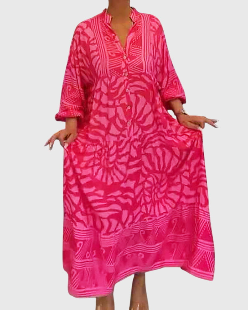 Pink - A woman wearing a vibrant pink and light pink abstract floral print maxi dress with long sleeves, a split V-neckline, and a tiered skirt featuring geometric border patterns.