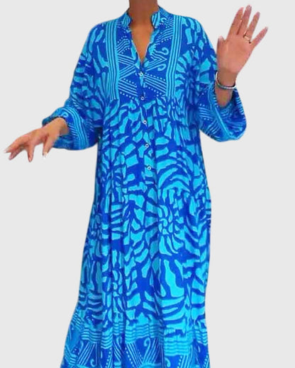 Blue - A woman wearing a vibrant pink and light pink abstract floral print maxi dress with long sleeves, a split V-neckline, and a tiered skirt featuring geometric border patterns.