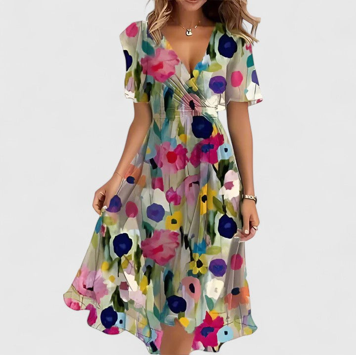 Beige Color Floral - A woman wearing a V-neck midi dress featuring a vibrant blue and green abstract mosaic print, short flutter sleeves, and a flowing A-line skirt.