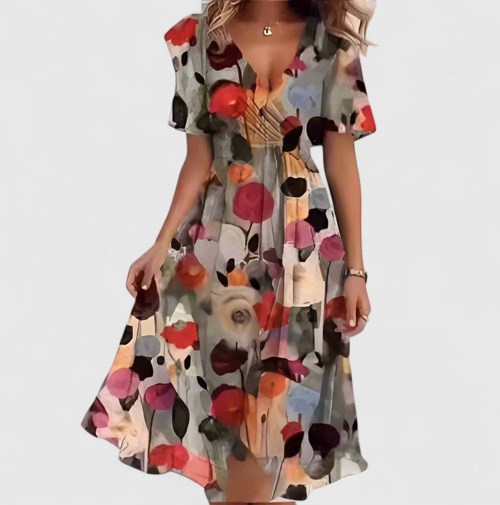 Brown Floral - A woman wearing a V-neck midi dress featuring a vibrant blue and green abstract mosaic print, short flutter sleeves, and a flowing A-line skirt.