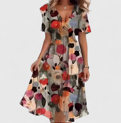 Brown Floral - A woman wearing a V-neck midi dress featuring a vibrant blue and green abstract mosaic print, short flutter sleeves, and a flowing A-line skirt.