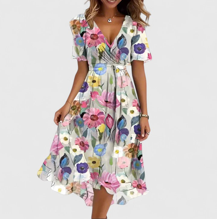 White Floral - A woman wearing a V-neck midi dress featuring a vibrant blue and green abstract mosaic print, short flutter sleeves, and a flowing A-line skirt.