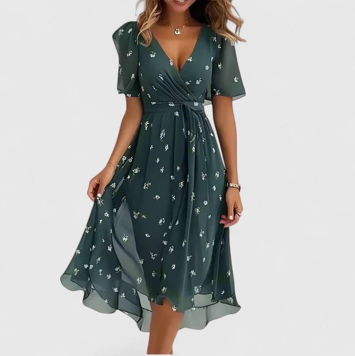 Green - A woman wearing a V-neck midi dress featuring a vibrant blue and green abstract mosaic print, short flutter sleeves, and a flowing A-line skirt.