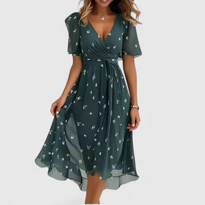 Green - A woman wearing a V-neck midi dress featuring a vibrant blue and green abstract mosaic print, short flutter sleeves, and a flowing A-line skirt.
