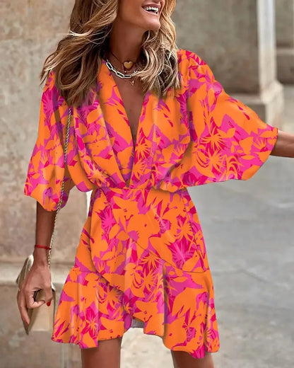 Orange - A woman wearing a vibrant, multi-colored abstract print mini dress featuring a deep V-neckline, wide kimono sleeves, and a draped wrap skirt.
