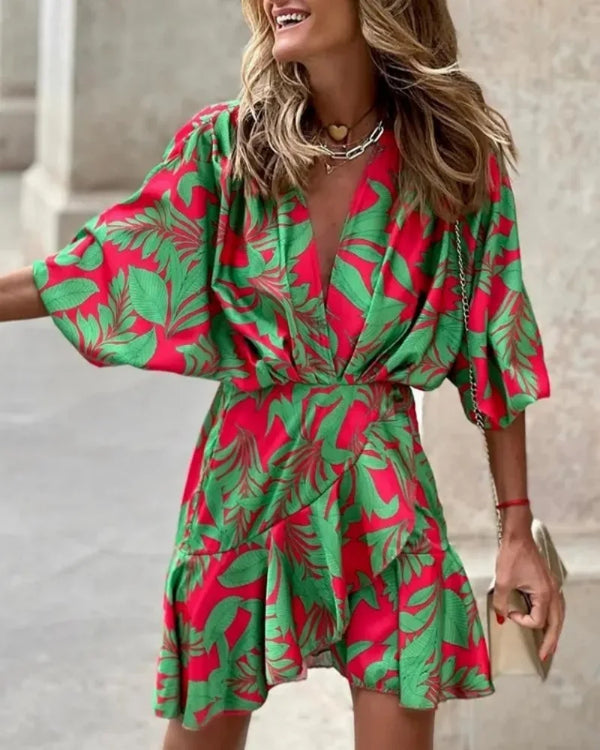 Green - A woman wearing a vibrant, multi-colored abstract print mini dress featuring a deep V-neckline, wide kimono sleeves, and a draped wrap skirt.