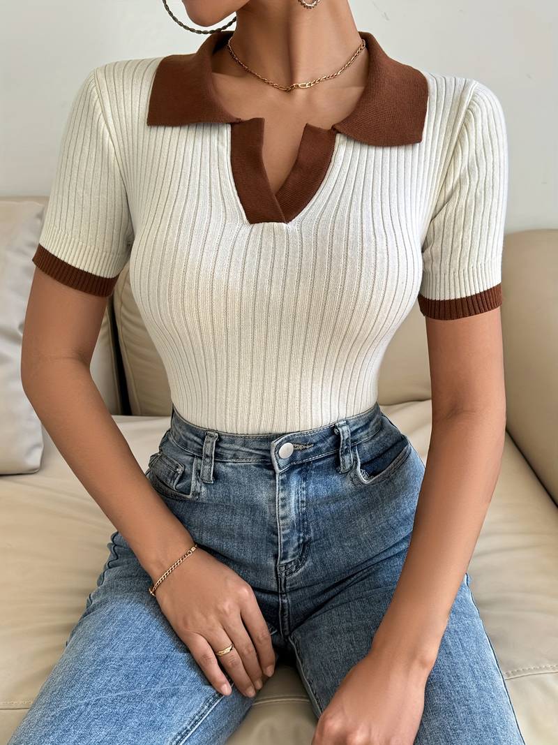 Woman in cream ribbed knit polo shirt with brown trim detail holding a white cup.