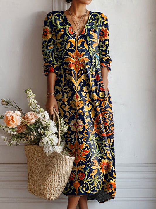 4XL - A woman wearing a long-sleeved, V-neck maxi dress featuring a vibrant blue, orange, and yellow Art Nouveau botanical print, holding a straw basket filled with flowers.