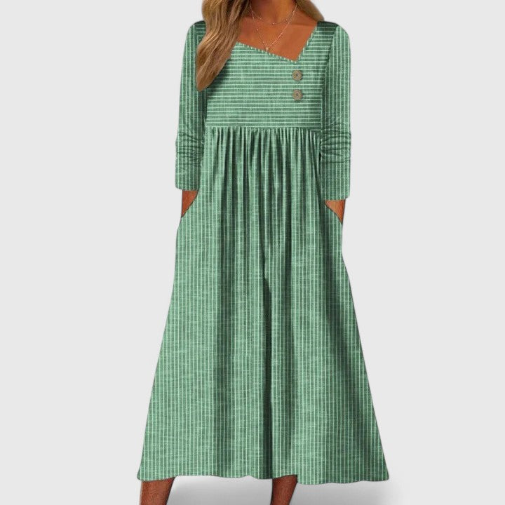 Green - A woman wearing a gray and white vertically striped midi sundress with three-quarter sleeves, an asymmetric neckline featuring two decorative buttons, an empire waist, and side pockets.