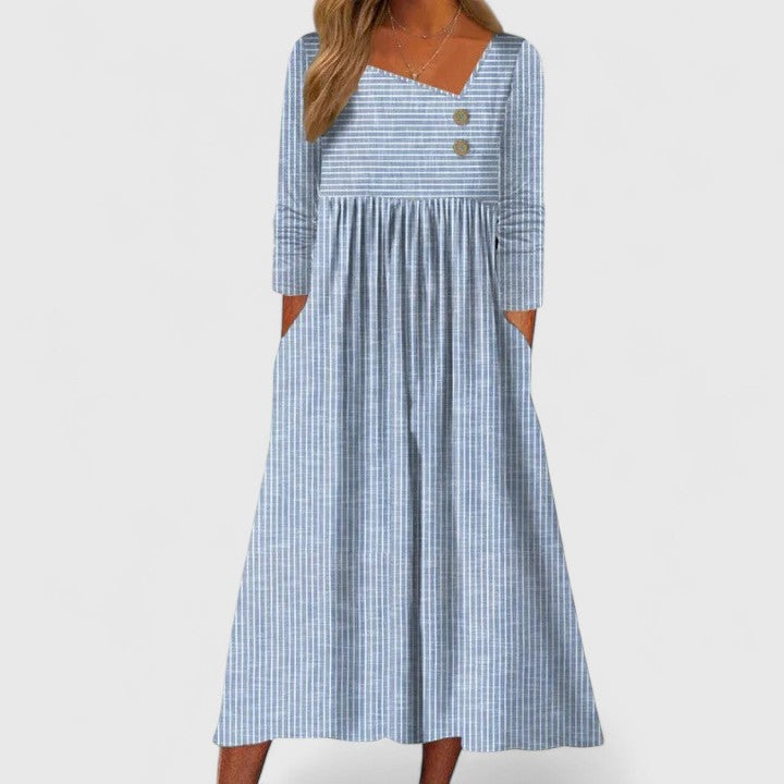 Blue - A woman wearing a gray and white vertically striped midi sundress with three-quarter sleeves, an asymmetric neckline featuring two decorative buttons, an empire waist, and side pockets.